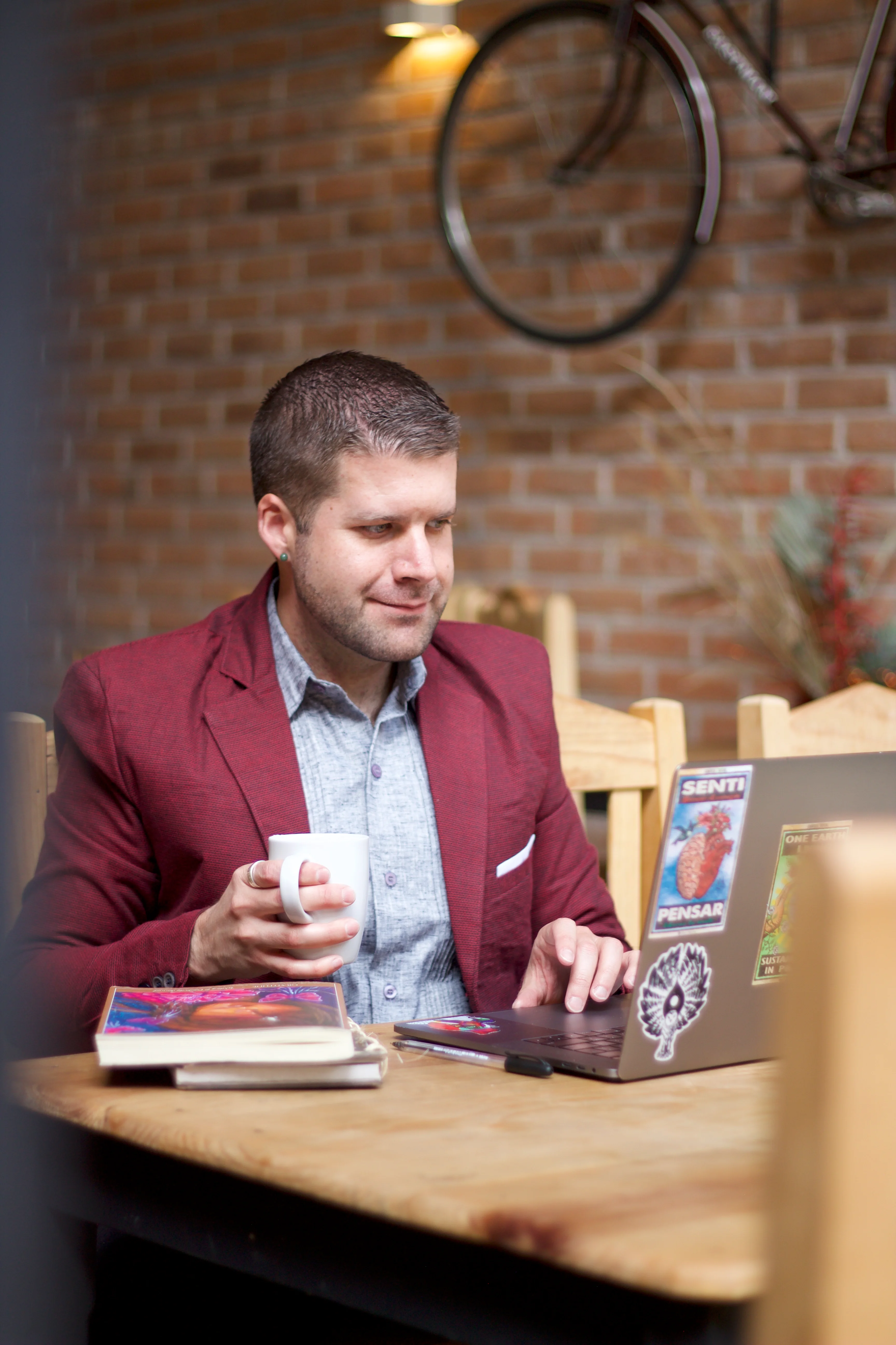 Grant James working remotely in a cafe with a cup of coffee in hand and a laptop, wearing a Burgundy suit.